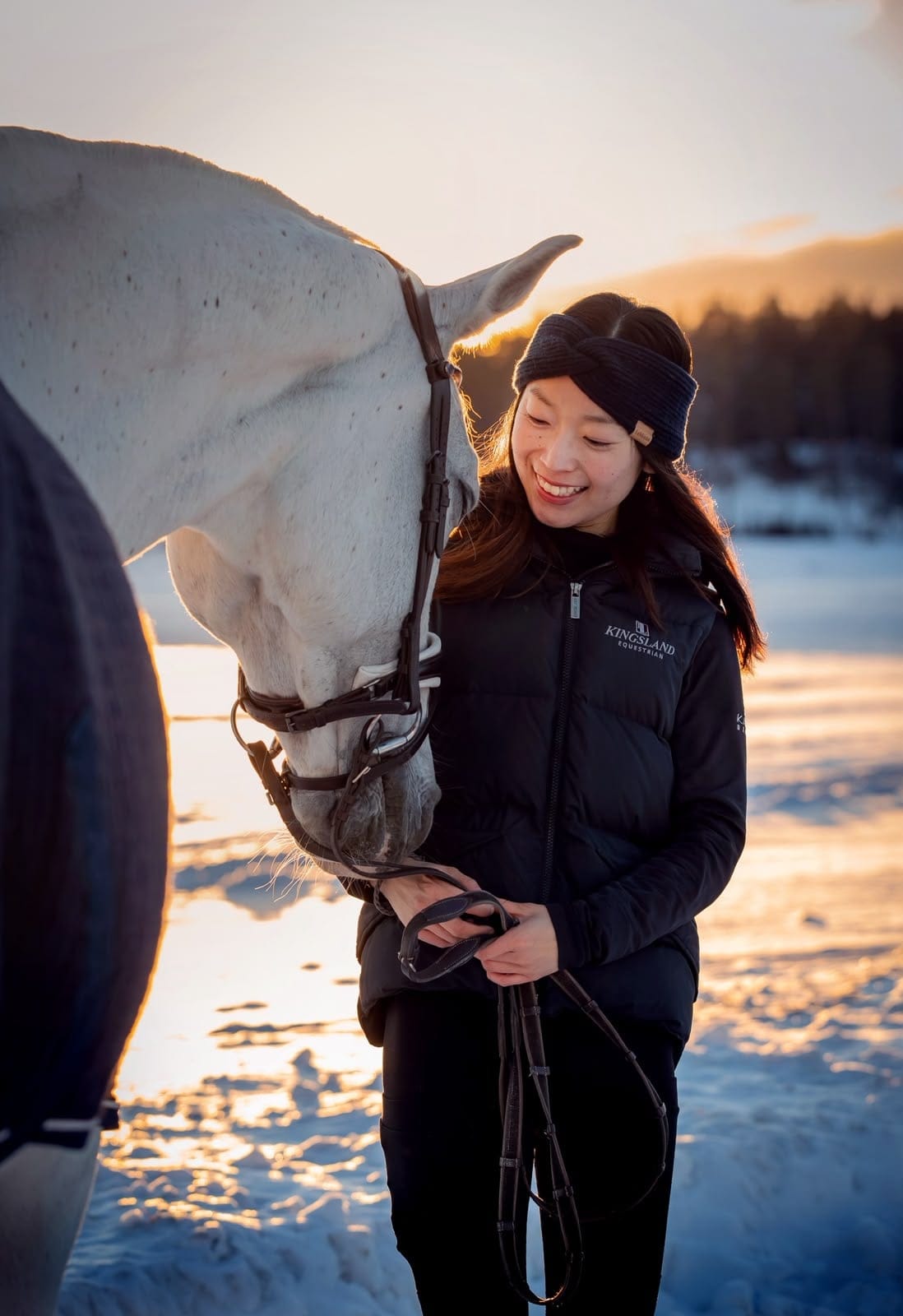 Yuka with a grey horse in the snow at sunset