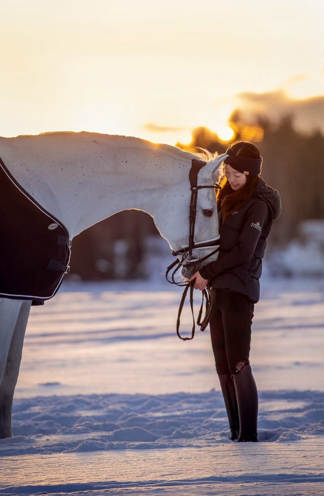 Yuka and a grey horse in a snowy field at sunset