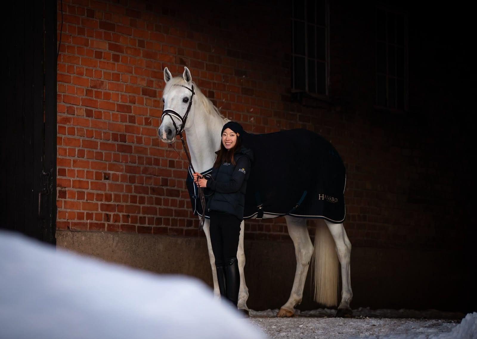 Yuka leading a grey horse out of the stable