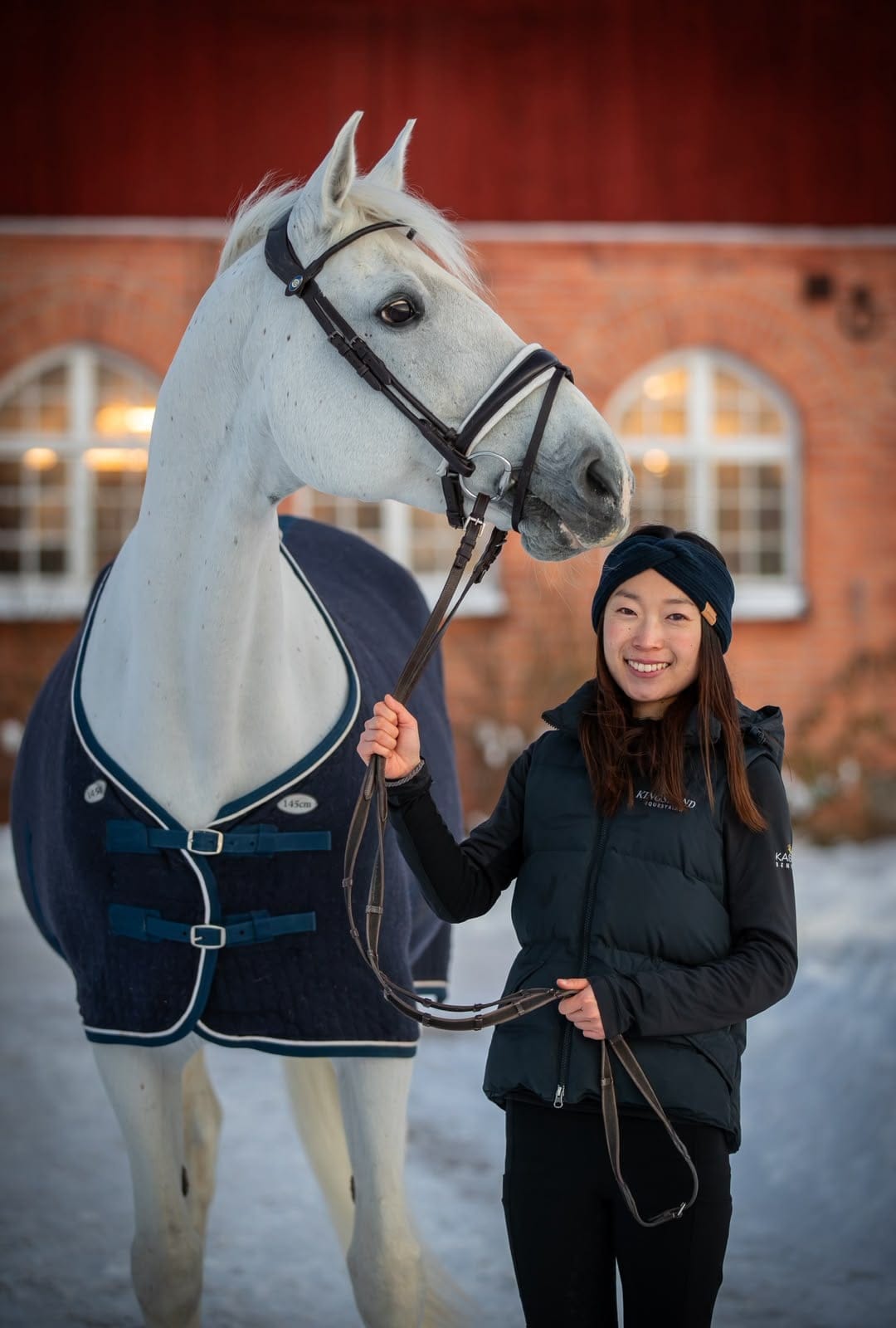 Yuka with a grey horse in front of a red brick stable