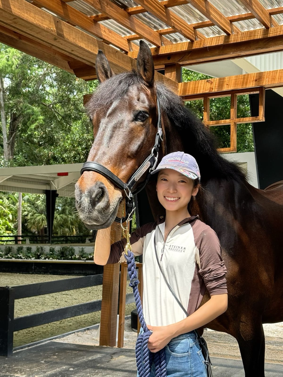 Yuka smiling next to a bay horse in the stable